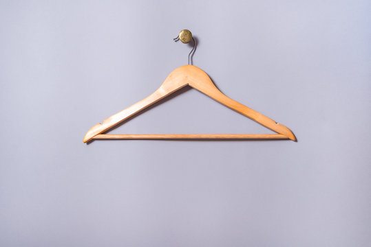 Empty wooden  lacquered clothes hanger hang on gray  wall, on brass cnob