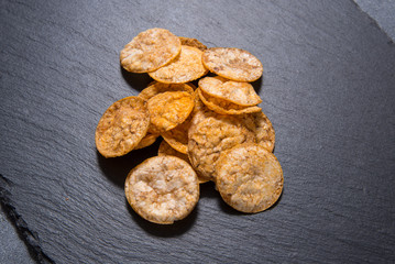 Top view pile of organic, crispy, baked, whole grain rice chips with spices. Gluten free healthy snack. On black sliced stone background