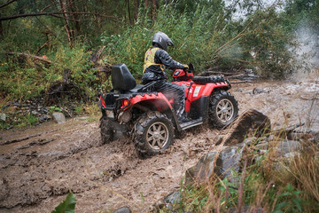 Quad rider jumping on a muddy forest trail.