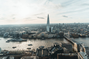 Naklejka premium Aerial view of London with The Shard skyscraper and Thames river at sunset with grey clouds in the sky. Financial district in the center of London from the viewing platform at Sky Garden.
