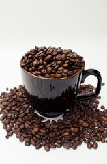 Close up on dark coffee mug overflowing with whole coffee beans