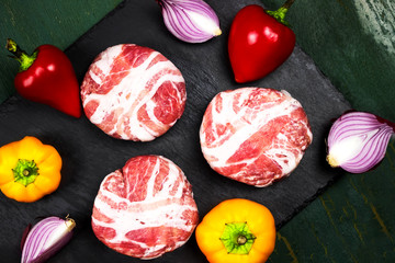 Meat raw round cutlets wrapped in bacon and vegetables onion, sweet pepper, garlic on a black stone background. The ingredients for the burgers. The view from the top. The concept of meat-lovers