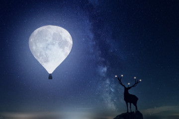 Fototapeta na wymiar Hirsch steht vor einem Mond mit der Form eines Ballon. Hintergrund Milchstraße