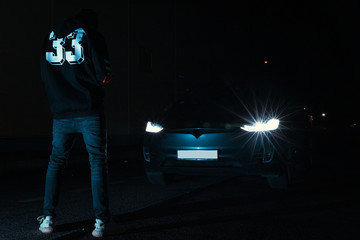 Young man standing in front of his car during the night 