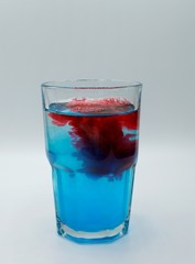 Glass of water with burst of blue and red color from water enhancer to make purple