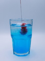 Glass of water with burst of blue and red color from water enhancer to make purple