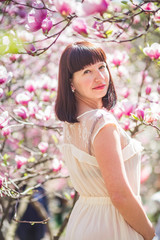 Fototapeta premium Beautiful woman among branches of magnolia in spring in park. Happy Woman on background of pink magnolias in Kiev.