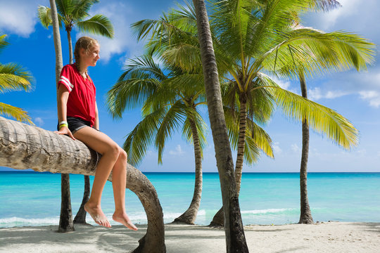 Happy teenage girl sitting on inclined palm tree on the beach of Saona island, Dominican Republic
