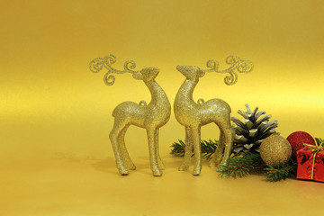 Figurki złotego jeloneka i bombki choinkowe na złotym tle, Boże Narodzenie.	