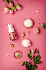 Homemade spa with rose cosmetic set, cream, rose water on pink background top view