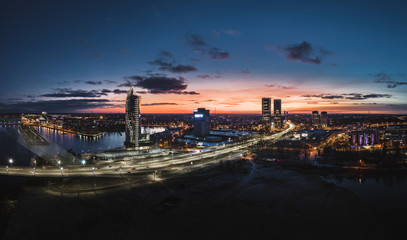 Aerial view over Riga city at night time. Urban landscape with skyscrapers and highway with city...