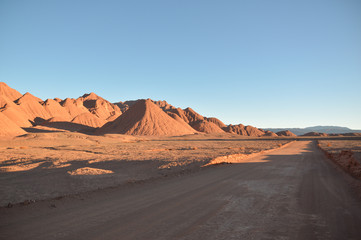 Fototapeta na wymiar Straight dirt road on the right and mountains on the left at the sunset. Puna labyrinth, Argentina