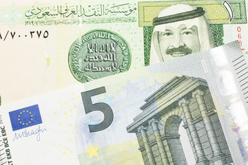 A green one riyal bank note from Saudi Arabia with a blue and green five euro bank note close up in macro