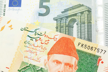 An orange and green twenty Pakistani rupee bank note with a red one hundfive Euro bank note in macro