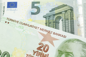 A close up image of a red, yellow and green twenty Turkish lira bank note with a German five euro bill in macro