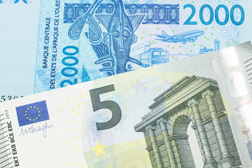 A close up image of a blue, West African franc bank note with a five Euro bank note in macro