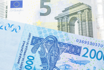 A close up image of a blue, West African franc bank note with a five Euro bank note in macro