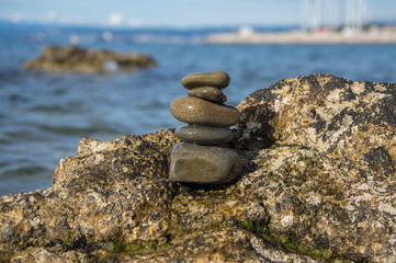 Five stones cairn tower, rock zen sculpture, brown beige pebbles on the rock and sea light blue background