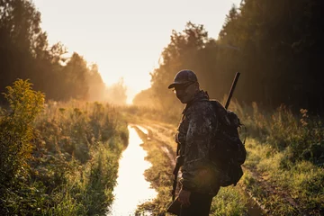 Foto op Canvas Summer hunting at sunrise. Hunter moving With Shotgun and Looking For Prey. © romankosolapov