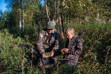 Two hunters father and son are eating together in the forest. Bushcraft, hunting and people concept