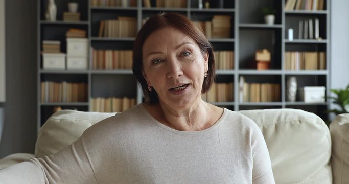 Mature older woman looking talking to camera sit on sofa