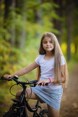 Obraz premium Cute little teenager girl riding bicycle in a sunny park