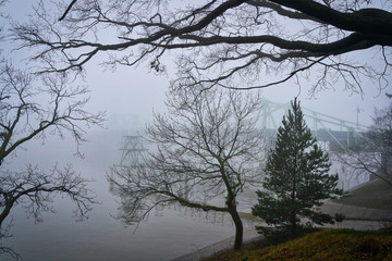 Thick dense fog with poor visibility on a cold winter morning. In the background are the metal structures of the bridge.