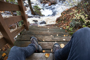 Man sitting down on stairway down to rapids in Autumn forest