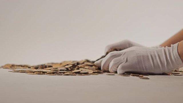White-gloved hands scooping up a pile of gold coins. They sort out and scatter money.On white background. Garland. Money glitters.