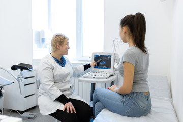 Obraz premium the doctor advises the patient girl after an ultrasound diagnosis. indicates with a pen on the monitor of the ultrasound machine the problematic place to which the patient should pay special attention