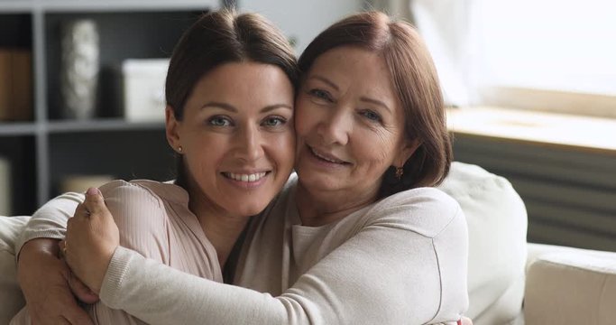 Loving older mum and young daughter cuddling looking at camera