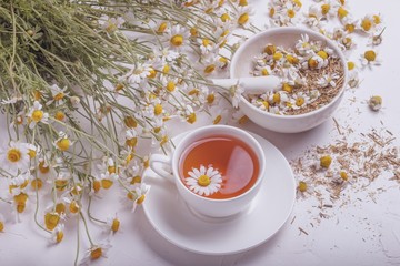 Rural still-life - cup of brewed chamomile tea on the background of a bouquet of daisies, closeup