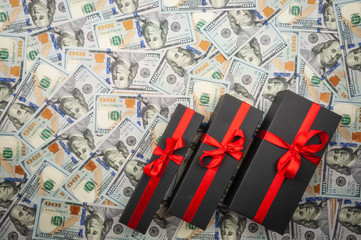 Three black gift boxes with bow on background of dollars. top view, copy space