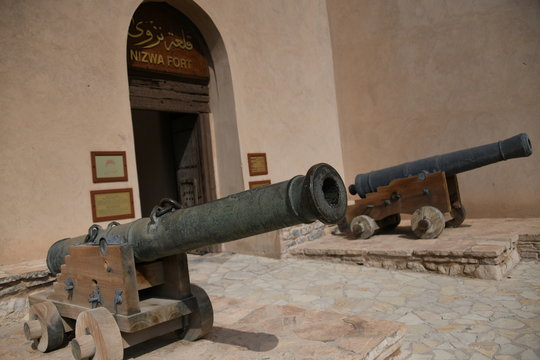 Die gro&szlig;e Ferstung das Fort Nizwa liegt am Rande des Hadschar Gebirge in der Oasenstadt im Oman. Am Eingang der Festung stehen zwei antike Kononen. 