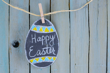 Hand drawn Easter egg, chalk on chalkboard with greeting hanging from twine by clothespin in front...