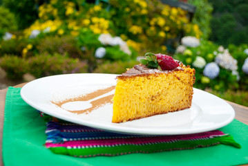 Portion of cake made with corn, dessert made in Guatemala, served outdoors on wooden table with ornaments made with cinnamon powder and strawberry.