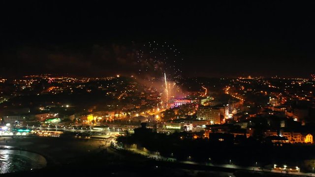 Aerial, drone shot, towards fireworks at the coast of Lisbon, at night time, New year evening, in Estoril, Portugal