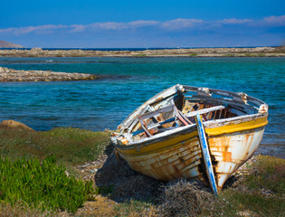 abandoned wooden fish boat at the shore. The boat is destroyed and rusty an completely useless with the sea and the blue sky at the background. Horizontal photo