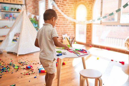 Beautiful african american toddler playing with cars around lots of toys at kindergarten