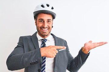 Young handsome business man wearing suit and tie and bike helmet over isolated background amazed and smiling to the camera while presenting with hand and pointing with finger.