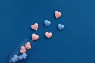 pink and one blue meringue hearts in transparent glass goblet and scattered on classic blue background diagonally, copy space