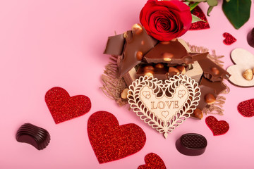 Valentine's day background with red hearts, chocolate candies and red rose on a pink background. Romantic atmosphere. Love symbols.