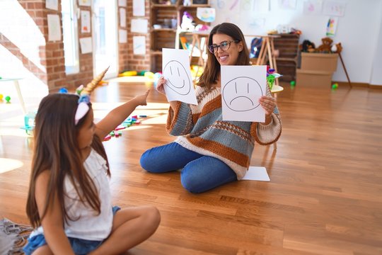 Beautiful pshychologist and toddler doing therapy with emotions emoji around lots of toys at kindergarten