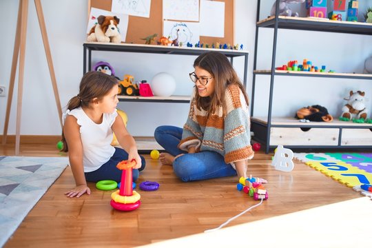 Beautiful teacher and toddler building pyramid using hoops around lots of toys at kindergarten