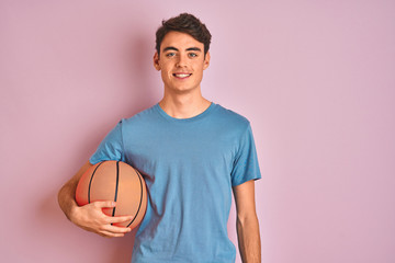 Teenager boy holding professional basket ball over isolated pink background with a happy face...