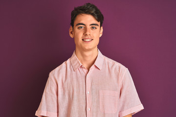 Fototapeta premium Teenager boy wearing pink shirt standing over purple isolated background looking away to side with smile on face, natural expression. Laughing confident.