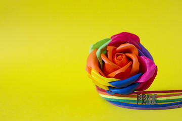 Rose of rainbow color on a yellow background and rainbow bracelet with the inscription Pride. LGBT concept