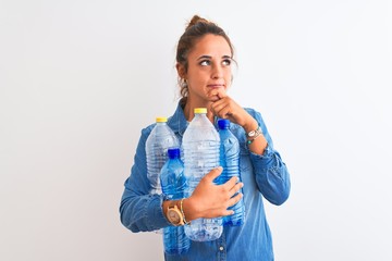 Young redhead woman holding plastic bottle to recycle over isolated background serious face...