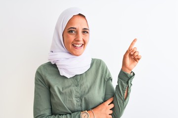 Young beautiful Arab woman wearing traditional Muslim hijab over isolated background with a big smile on face, pointing with hand and finger to the side looking at the camera.
