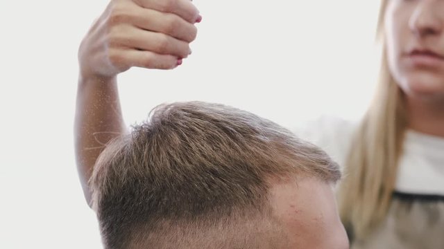A stylist is using a spray. A client has brown hair. The hairdresser is doing a hairstyle for the client.